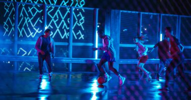 Genç siyahi adam çeşitli arkadaşlarıyla futbol oynuyor. Çok Irklı Stylish Grubu Çatıdaki Neon Urban Stpot 'ta Futbol Oyununun keyfini çıkartıyor