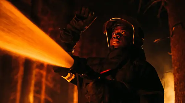 stock image Close Up Low Angle Creative Portrait of a Brave African American Firefighter Using a Firehose to Fight a Forest Fire. Black Fireman Holds High