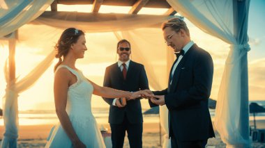 Güzel Gelin ve Damat Sunset 'te bir Ocean Beach' te Açık Hava Düğün Töreni sırasında. Evlenmek, Yüzük Değiştirmek, Öpüşmek İçin Mükemmel Bir Yer