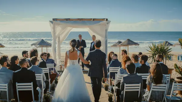 stock image Beautiful Bride in White Wedding Dress Going Down the Aisle with Her Father, while Groom Waits at an Outdoors Ceremony Venue Near the Sea with Happy