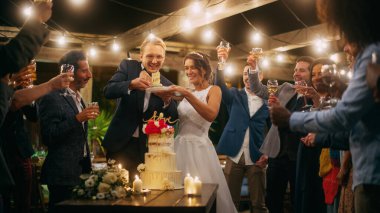 Güzel Gelin ve Damat, Çoklu Etnik Arkadaşlarla Akşam Resepsiyonunda Düğünü Kutluyor. Evli çift yemek masasında durur, öpüşürler.