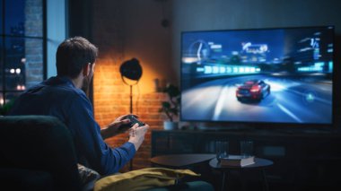 Genç adam evde vakit geçiriyor, lüks bir dairede bir koltukta oturuyor ve konsolda Arcade Car Video Oyunları oynuyor. Erkek Denetleyici Kullanan