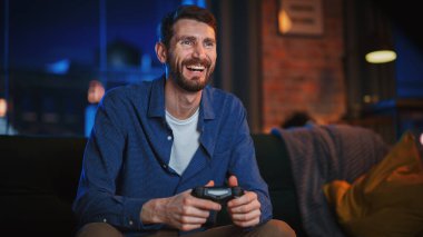 Genç Yakışıklı Adam 'ın Evde Zaman Geçirmesi, Stylish Loft Apartmanında Bir Koltukta Oturması ve Konsolda Video Oyunları Oynaması. Başarılı Erkek