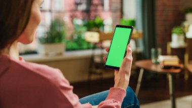 Yeşil Ekran Mock Up ekran ile Kadın Eli Akıllı Telefonu Tutuyor. Kadın Evde Rahatlıyor, Video İzliyor ve Sosyal medya paylaşımları okuyor