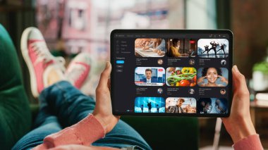 Kadın Eli Ekranda Video Yayını Servisi ile Tablet Tutuyor. Kadın Evdeki Koltukta Rahatlıyor, Video İzliyor ve Sosyal Bilgiler Okuyor