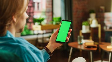 Yeşil Ekran Mock Up Ekranlı Akıllı Telefon Tutan Adam. Erkek Evde Dinleniyor, Video İzliyor ve Mobil Aygıtta Sosyal Medya Gönderileri Okuyor