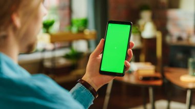 Yeşil Ekran Mock Up Ekranlı Akıllı Telefon Tutan Adam. Erkek Evde Dinleniyor, Video İzliyor ve Mobil Aygıtta Sosyal Medya Gönderileri Okuyor