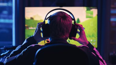 Head View: Genç Kadın Profesyonel Oyuncu Kulaklığa Oturdu ve Neon Lit Salonunda Kişisel Bilgisayarda Bir Video Oyunu Oynamaya Başladı