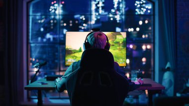 Back View: Profesyonel Kadın Oyuncu Evdeki Neon Lit Salonunda Kişisel Bilgisayarda Bir Video Oyunu Oynuyor. Kız Şampiyonluğu Kazanmaya Hazır