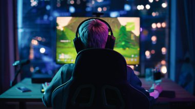 Back View: Profesyonel Kadın Oyuncu Evdeki Neon Oturma Odasında Kişisel Bilgisayarda Bir Video Oyunu Oynuyor. Kız Turnuvayı Kazanmaya Hazır. Şık