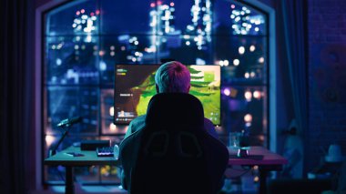 Arka Görünüm: Profesyonel Başarılı Kadın Oyuncu Kulaklık Takıyor ve Evde Neon Lit Oturma Odasında Kişisel Bilgisayarda Bir Video Oyunu Oynuyor