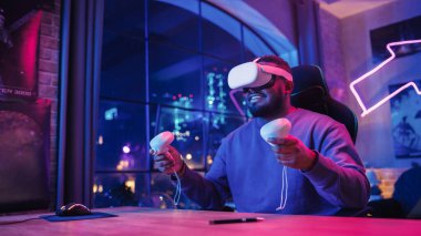 Stylish Man Using Virtual Reality Headset with Controllers at Home in Loft Apartment. Young African American Male Surfing the Web, Spending Time in VR clipart