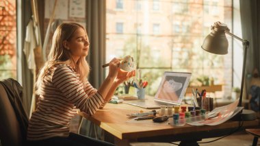 Masasının arkasında oturan, çizim yapan, özel yapım spor ayakkabıları üzerinde çalışan genç bir kadın. Profesyonel Kadın Sanatçı Eski Ayakkabılar Üzerine Kendi Tasarımını Uyguluyor