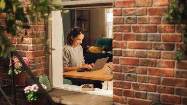 İspanyol kadın dizüstü bilgisayar kullanıyor ve dairesinde oturma odasında oturuyor. Profesyonel Kadın Uzaktan Çalışıyor Çevrimiçi, Planlama, Beyin Fırtınası