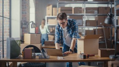 Küçük işletme sahibi, Depo 'daki masasında dururken dizüstü bilgisayarda çalışıyor. Personel odasında şık bir Retro Bisiklet Koltuğu Paketliyor