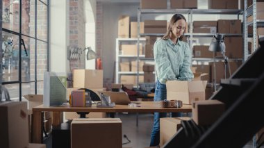 Çevrimiçi Dükkan Satış Yöneticisi Laptop Bilgisayar kullanarak, Postaya Küçük bir Paket Hazırlıyor. Genç Sevimli Teslimat Servisi Elemanı Almaya Geldi