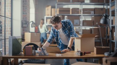 Küçük işletme sahibi, Depo 'daki masasında dururken dizüstü bilgisayarda çalışıyor. Personel odasında şık bir Retro Bisiklet Koltuğu Paketliyor