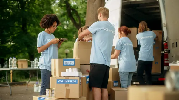 Stock image Group of Hardworking Volunteers Preparing Donated Free Food Rations, Loading Packages in a Cargo Van on a Sunny Day. Charity Workers Work in Local