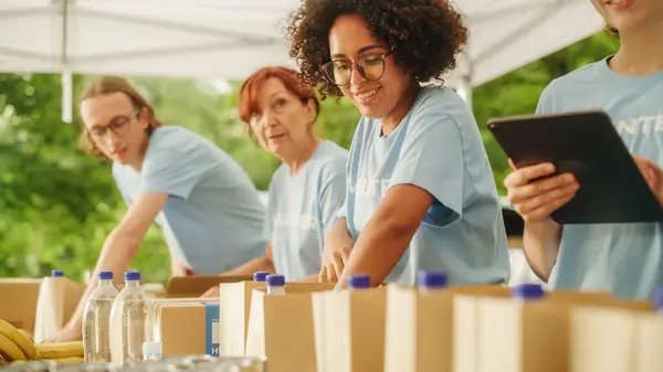 stock image Portrait of a Happy Young Black Female Preparing Free Food Rations Together with Other Volunteers. Charity Workers and Members of the Community Work