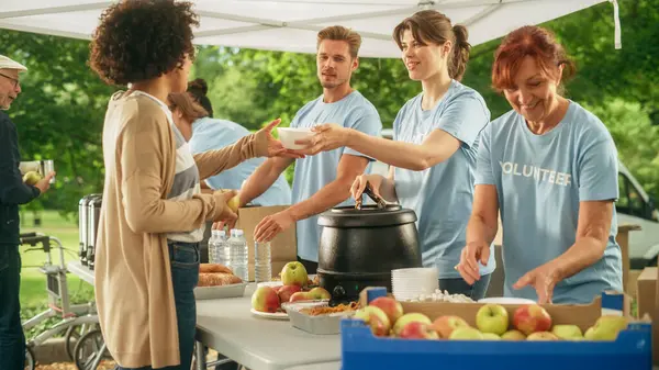 Stock image The Concept of Giving: Homeless People Reach Out To Free Volunteer Meals from Multiethnic Team of Volunteers. Humanitarian Aid Charity Workers Serve