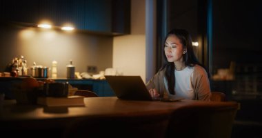 Cozy Kitchen 'da Masada Oturan Güzel Otantik Asyalı Kadın ve Geceleri Evde Dizüstü Bilgisayar Kullanmak. Kadın Gülümseyen ve Konuşan