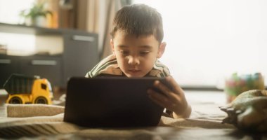 Parlak Stylish Odasında dijital tablet kullanan Asyalı bir çocuğun portresi. Küçük şirin çocuk hafta sonunun tadını çıkarıyor, eğitici oyunlar oynuyor, resim çiziyor.