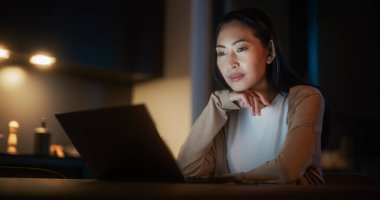 Cozy Kitchen 'da Masada Oturan Güzel Asyalı Kadın ve Geceleri Evde Dizüstü Bilgisayar Kullanmak. Sosyal Hizmetlerde Gülümseyen ve Konuşan Kadın