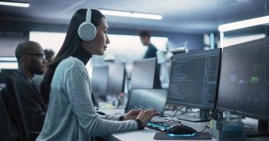 Teknoloji Ofisi 'nde Bilgisayar üzerine çalışan düşünceli genç bir mühendisin portresi. Güzel Asyalı kadın kulaklık takıyor, yazıyor.