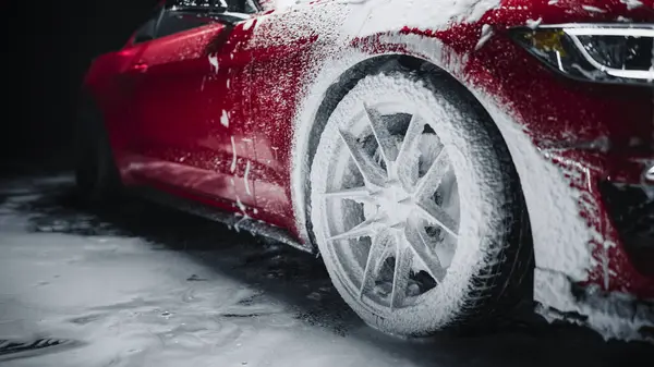 stock image Professional Car Wash Worker Applying Smart Foam on a Front Wheel of a Red Sportscar with Retro Design at a Dealership Car Detailing Center