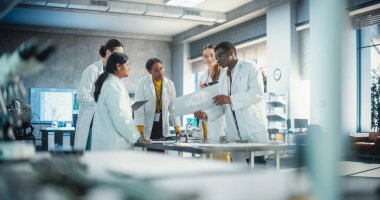 Endüstriyel Robot Uzmanlarından oluşan çeşitli bir ekip bir taslağı tartışmak için bir masanın etrafında toplandı. Laboratuar Önlüklü Mühendisler Dizüstü bilgisayar ve