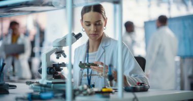 Bir girişim laboratuvarında çalışan çeşitli genç mühendisler grubu. Kadın Uzman Proje Yöneticileri Mikroskop Kullanırken Elektronik Devre Denetimi