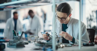 Bir girişim laboratuvarında çalışan çeşitli genç mühendisler grubu. Profesyonel Ekip Teknolojiyi Tartışırken Erkek Uzman Bir Devre Kurulunu lehimliyor