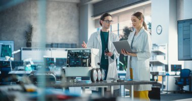 Mobil bir robot üzerinde çalışan iki endüstriyel robot uzmanı dizüstü bilgisayar kullanıyor. Laboratuvar Önlüklü Genç Erkek Mühendis Otomatik Yapay Zeka Robotunu Tartışıyor