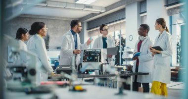 Çeşitli Endüstriyel Robot Uzmanları Mobil bir robotla bir masanın etrafında toplandı. Laboratuvar Önlüklü Mühendisler Otomatik Yapay Zeka Robotunu Tartışıyor