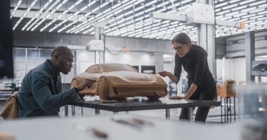 Genç Kadın Çırak Araba Modelcisi, modern elektrikli arabanın 3 boyutlu polimer Clay modelini yaratmak için siyahi yaşlı otomotiv tasarımcısıyla çalışıyor. Takım
