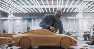 Afrikalı Araba Modelleyicisi Plastik Modelleme Clay 'den yapılmış konsept bir arabada yaratıcı çalışma sürecinin tadını çıkarıyor. Yakışıklı Siyah Tasarımcı Spatula kullanarak