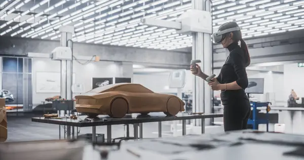 stock image Female Car Designer Wearing a Virtual Reality Headset and Using Controllers to Work on a Concept Car Made Out of Plasticine Modeling Clay. Talented