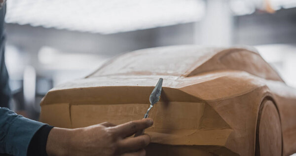 Close Up Portrait of an Automotive Designer Sculpting a 3D Clay Model of a Modern Sustainable Electric Car. Young Black Man Using a Spatula to