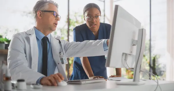 Doctors Office: Physician Talks With Professional Head Nurse, Using Computer. African Medical Health Care Specialist Discussing Test Results