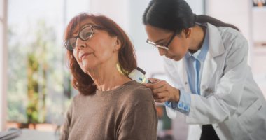 Genç bir Asyalı Dermatoloğun portresi Sağlık kontrolü sırasında kıdemli bir hastanın cildindeki hasarı incelemek için tıbbi büyüteç kullanıyor.