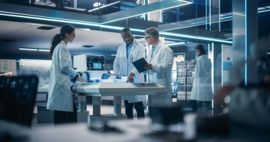 Çeşitli Endüstriyel Robot Uzmanları Mobil bir robotla bir masanın etrafında toplandı. Laboratuvar Önlüklü Mühendisler Otomatik Robotu Tartışıyor