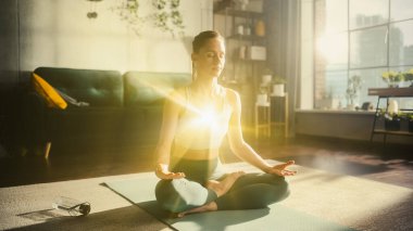 Lotus pozisyonunda güzel, rahat, beyaz bir kadın. Dairenin oturma odasında meditasyon yapıyor. Parlak Enerjinin Görüntülenmesi Düzenlendi