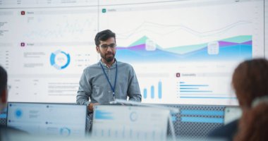 Tabletli Hintli Erkek Bilgisayar Bilimadamı, İzleme Odası 'ndaki Büyük Dijital Ekran Önündeki Çeşitli Veri Analistlerine Sunum Yapıyor
