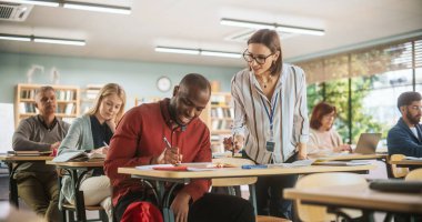 Genç öğretmen siyah bir erkeği kontrol ediyor, bir okul görevinde ona yardım ediyor, çalışmalarını övüyor. Modern Yetişkin Eğitim Merkezi İnsanların Geliştirilmesine Yardım Eder