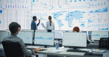 Siyah Erkek Analistin, Kafkas Kadın Yöneticisi ile Dünya Haritası Ofisi 'nde Büyük Dijital Ekran Önünde Konuşması. Çeşitli