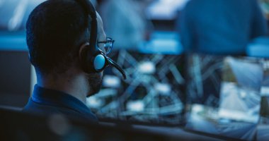 Teknik Müşteri Destek Uzmanı, Ekran Ekranları ve Ekranları Dolu Çağrı Merkezi Kontrol Odası 'nda bir bilgisayar üzerinde çalışırken Kulaklıkla konuşuyor