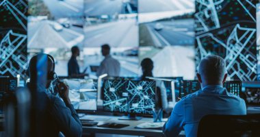 Masaüstü Bilgisayarları üzerinde çalışan çok ırklı uzmanlarla dolu karanlık oda. Büyük Dijital Ekran İzleme Uydu Verilerini, Şehir Haritasını ve CCTV Trafiğini Gösteriyor