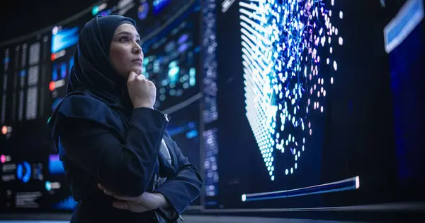 Stock image Portrait of a Smart Focused Middle Eastern Software Engineer Analyzing Neural Network Big Data on a Digital Screen. Young Arab Woman in Hijab Working