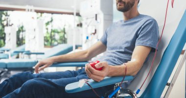 Eklenmiş bir kateterle erkek kan donörünün yakın çekimi. Kafkasyalı adam tüpten kan pompalamak için kalp şeklinde kırmızı top sıkıyor.