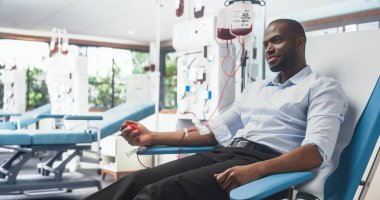 Parlak bir hastanede ihtiyacı olan insanlar için kan bağışı yapan siyah bir adam. Afrikalı erkek bağışçı, tüpten kan pompalamak için kalp şeklinde kırmızı top sıkıyor.
